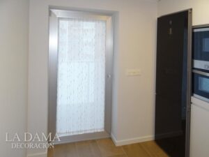 Cortina estirada en una puerta de cocna, tejido estirado y sujeto con portavisillos.